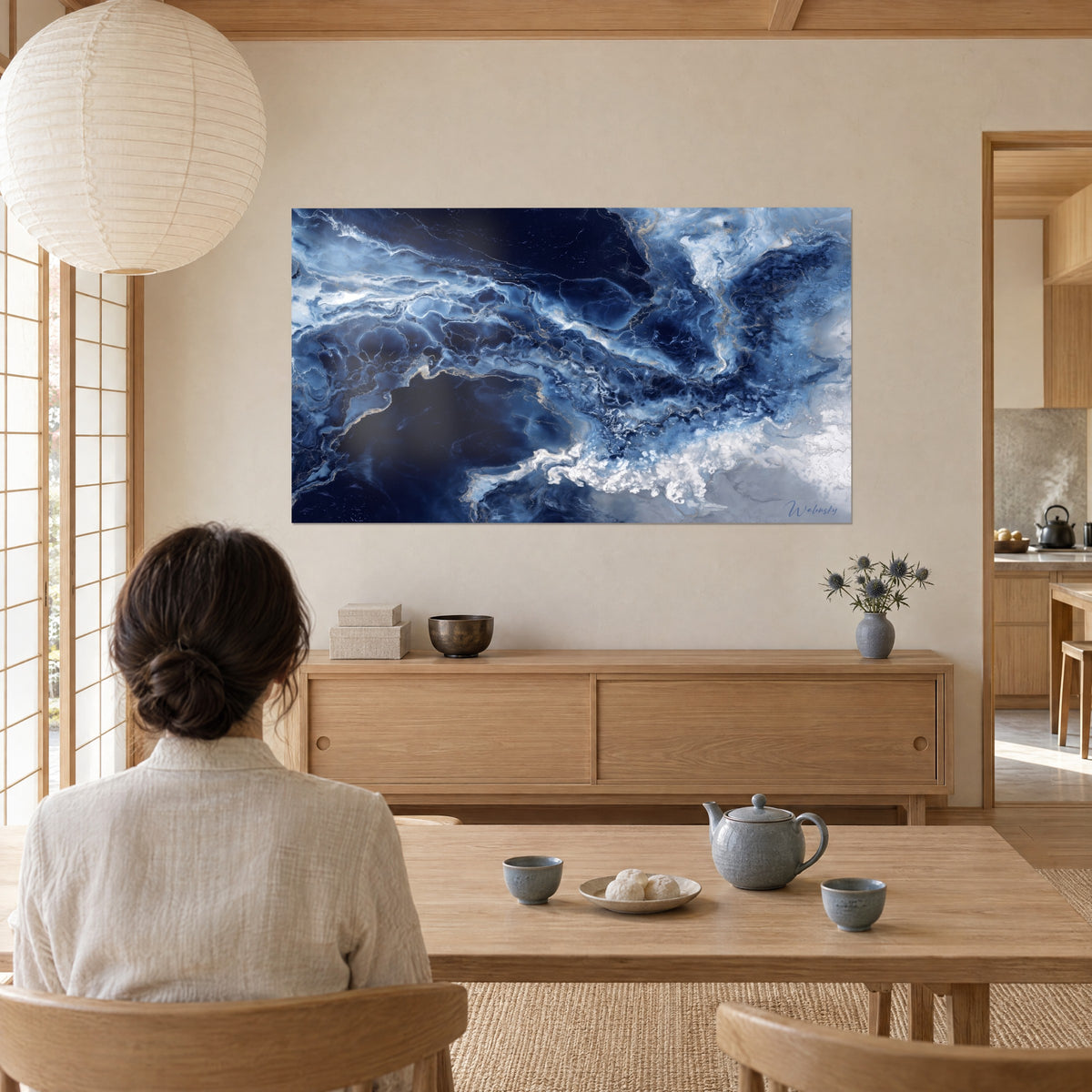 Cuadro olas de mármol azul real y plata, espuma blanca abajo a la derecha, mujer de espaldas junto a una mesa baja de madera