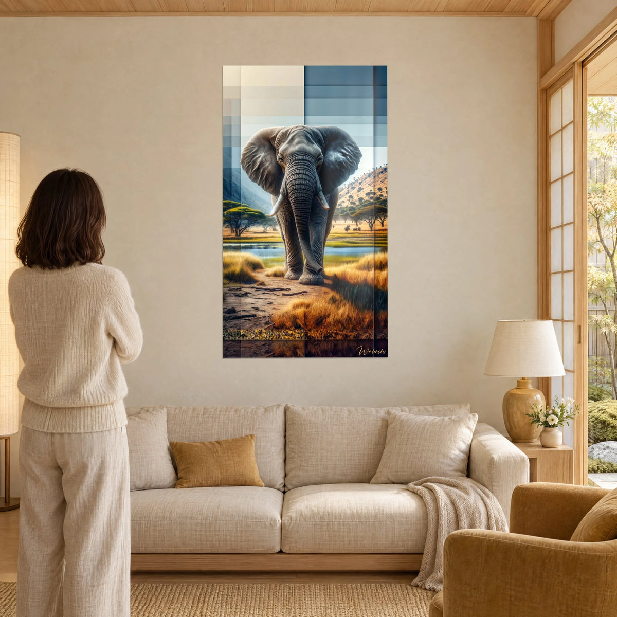 Wall art African elephant with ivory tusks, ochre savanna and steel-blue sky, woman seen from behind, above a sofa in a bright living room