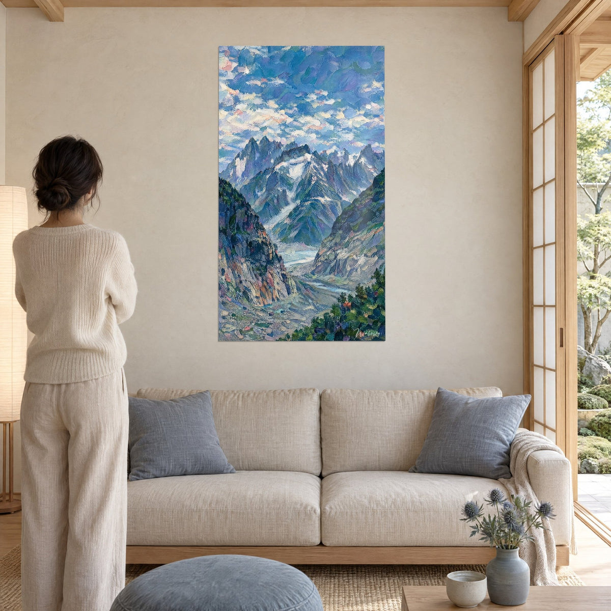 Tableau massif alpin aux aiguilles enneigées, ciel bleu et rose, femme de dos, au-dessus d'un canapé dans un salon lumineux