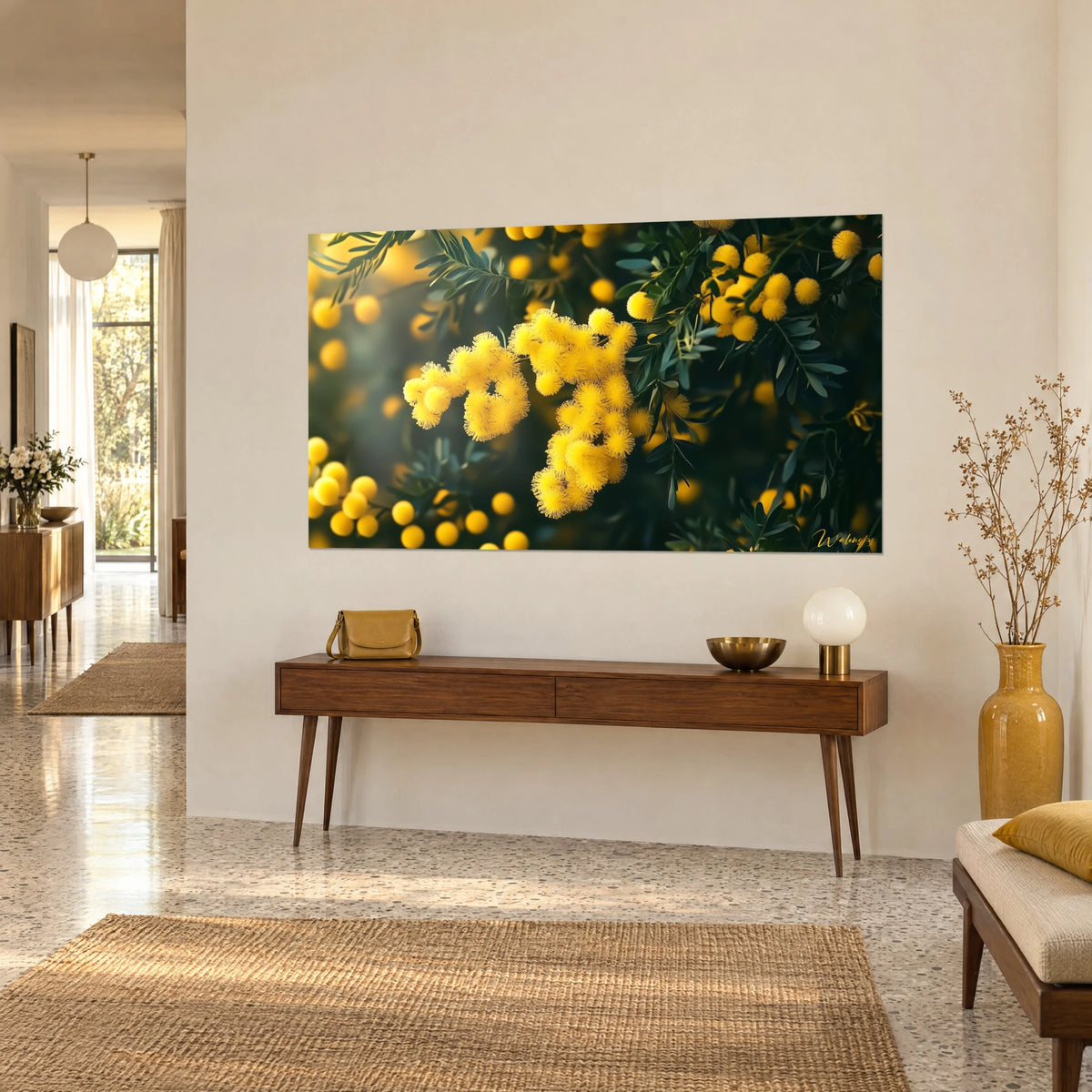 Quadro di ramo di acacia in fiore, pompon setosi giallo vivo e foglie verde profondo, su una parete beige accanto a una console in legno