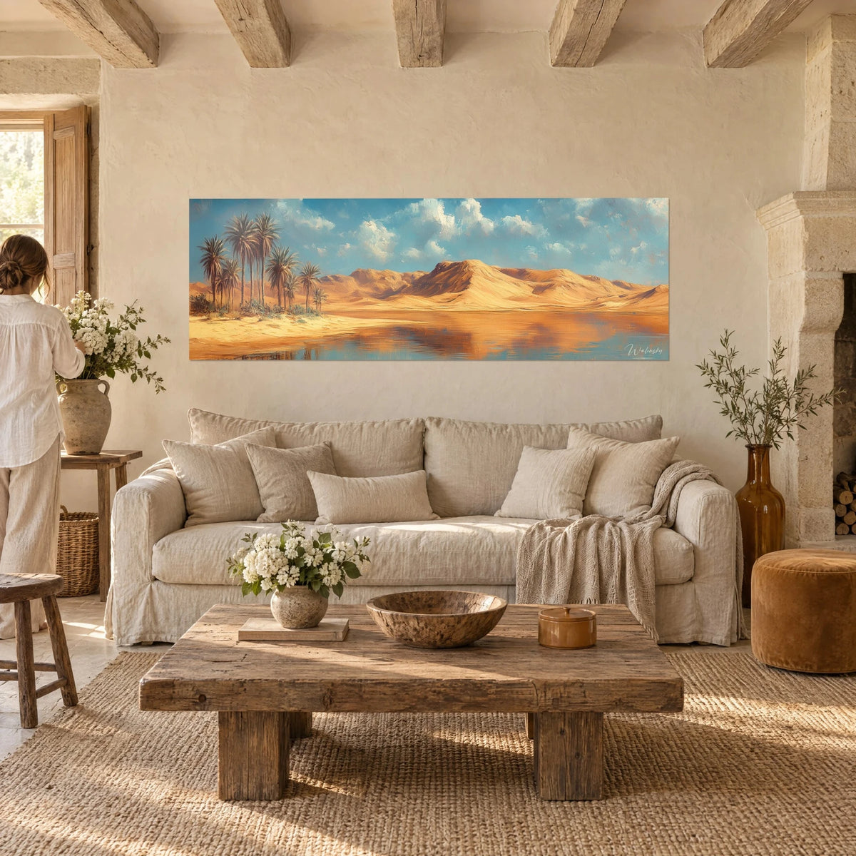 Quadro oasi di palme ai piedi di dune ocra, cielo azzurro punteggiato di nuvole, una donna di spalle, sopra un divano in un soggiorno luminoso