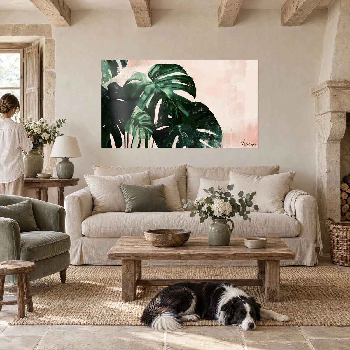 Wall art monstera with large fir-green leaves on a powdery pink background, above a sofa in a bright living room