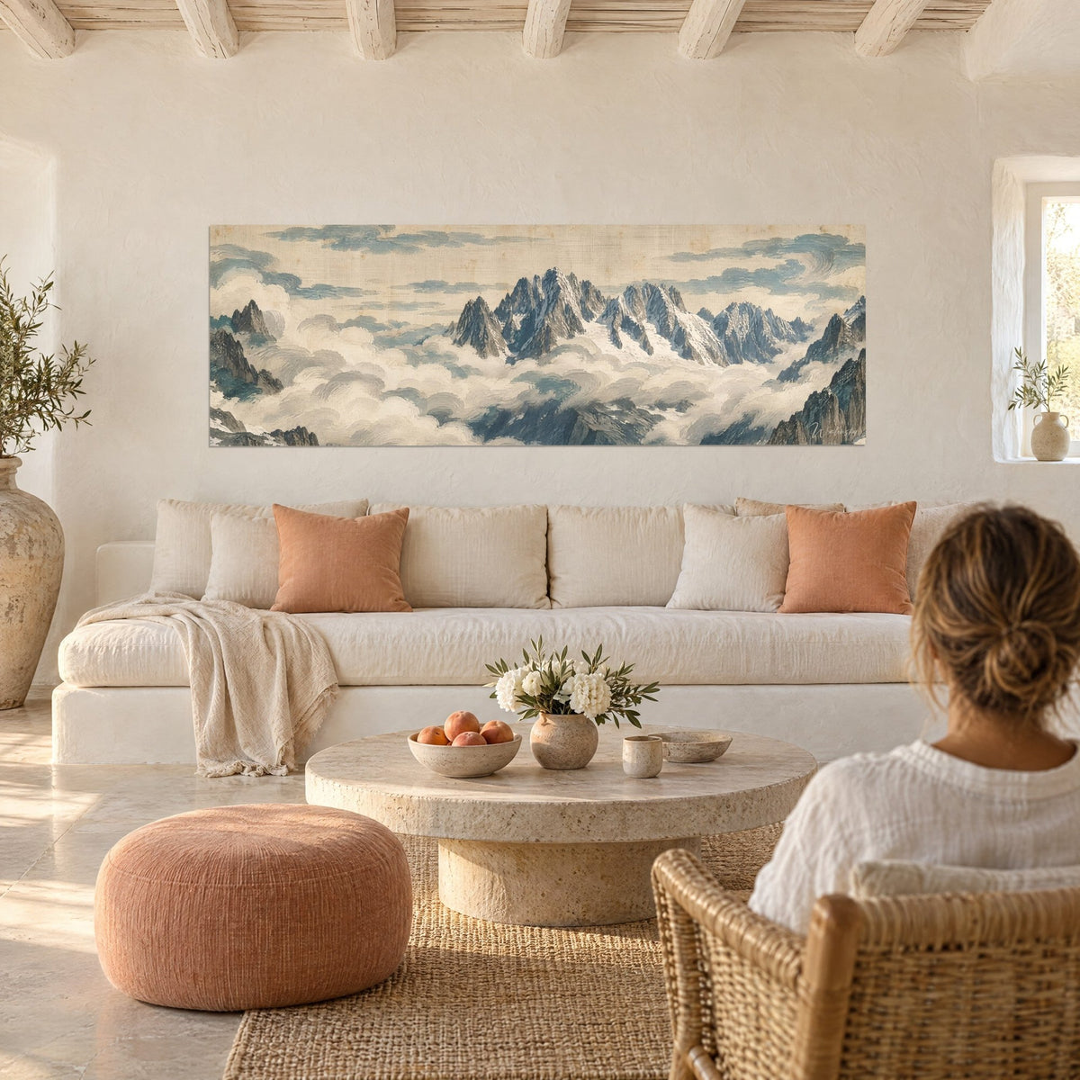 Wall art snow-capped peaks piercing a sea of clouds, slate blue and cream, woman seen from behind, above a sofa in a bright living room
