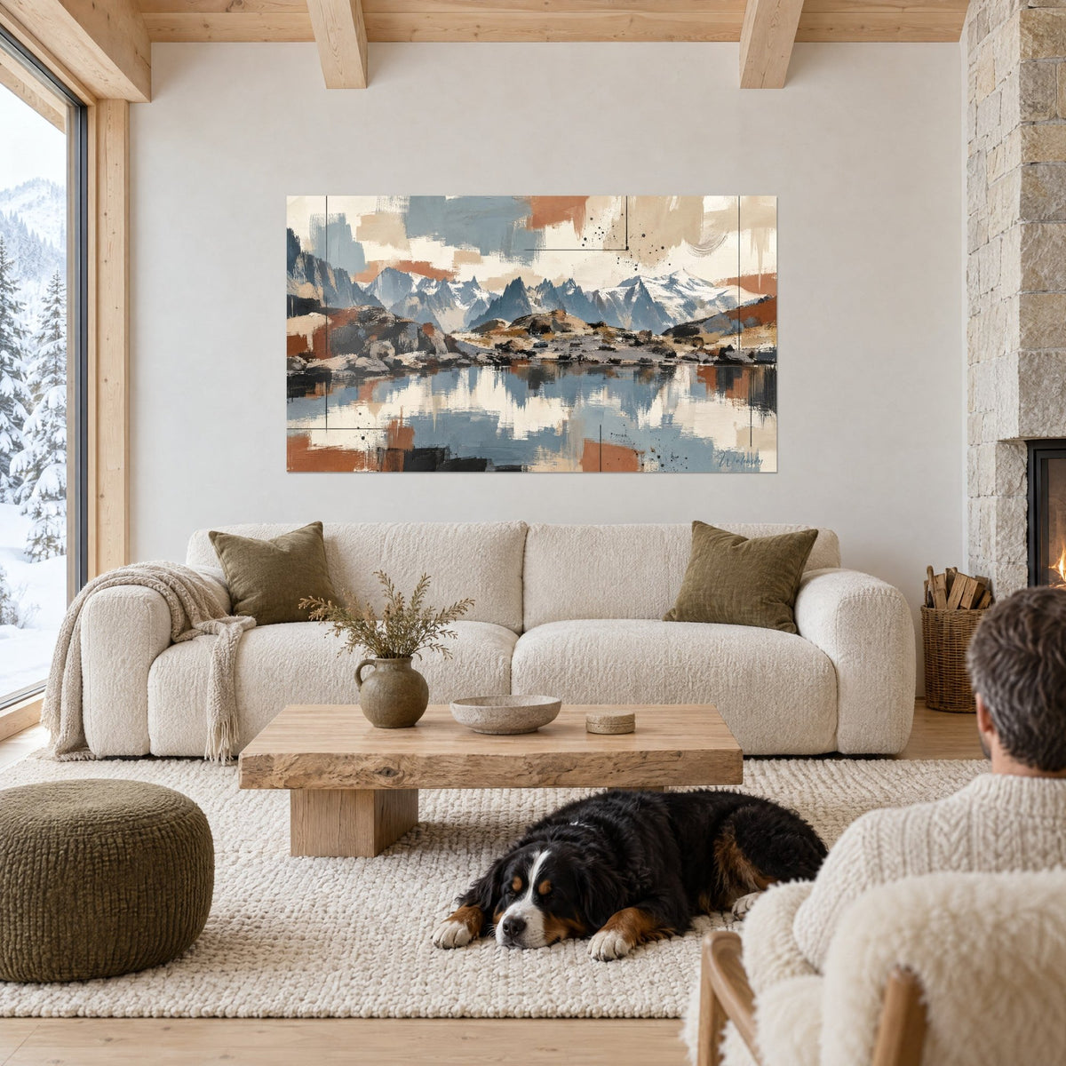Wall art of a snow-covered massif in slate blue and terracotta, reflected in a lake, black-and-white dog lying in front, above a sofa in a bright living room