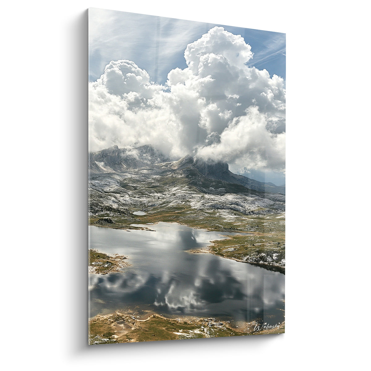 Lac glaciaire reflétant nuages blancs et montagnes grises sous ciel bleu pâle lumineux