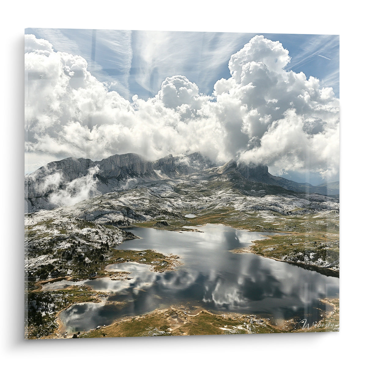 Sommets gris et nuages blancs cotonneux se reflètent dans un lac bleu pastel immobile