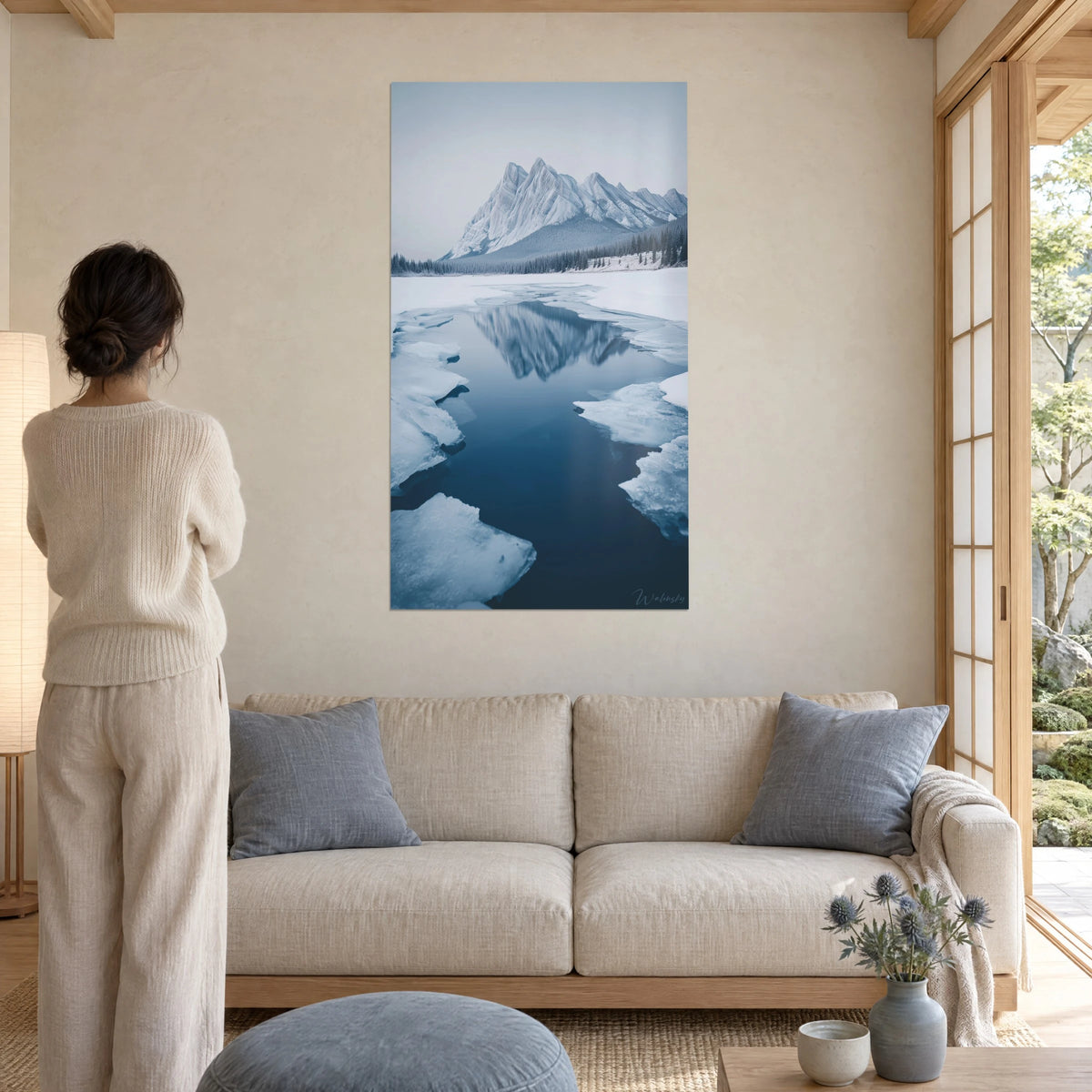 Tableau sommet enneigé en miroir sur un lac gelé, bleu nuit et blanc glacé, femme de dos, au-dessus d'un canapé dans un salon lumineux