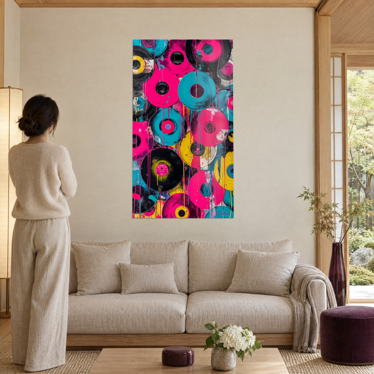 Tableau disques vinyles rose fuchsia et turquoise éclaboussés de jaune, femme de dos, au-dessus d'un canapé dans un salon lumineux