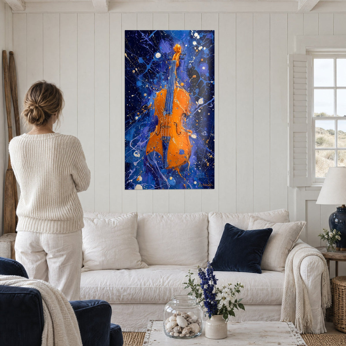 Tableau violon orange vernissé sur fond bleu nuit éclaboussé, femme de dos, au-dessus d'un canapé dans un salon lumineux