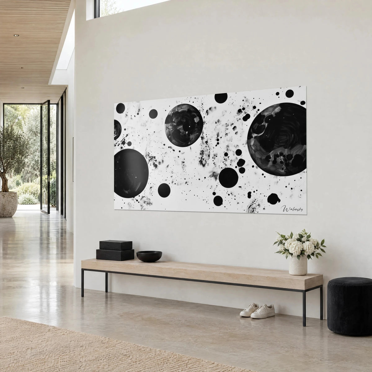 Quadro pianeti d'inchiostro nero, gocce sparse su fondo bianco crema, appeso sopra una panca in legno chiaro