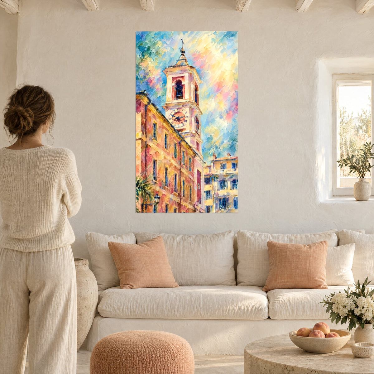 Quadro campanile con quadranti a numeri romani, facciate ocra e rosa sotto un cielo azzurro pastello, donna di spalle, sopra un divano in un soggiorno luminoso