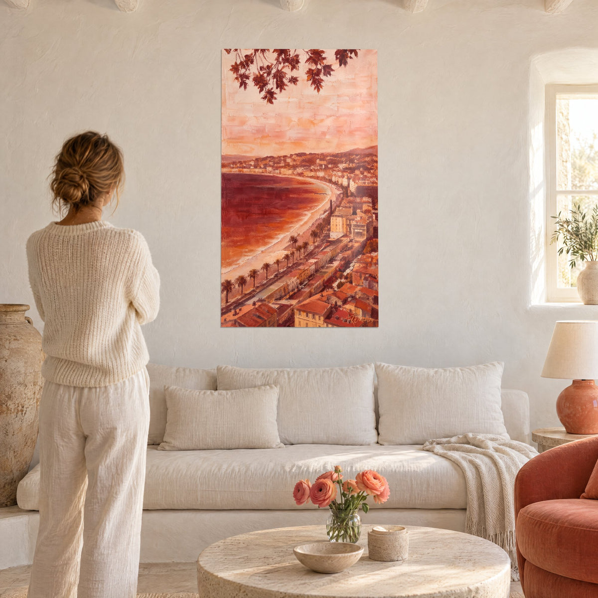 Wall art of the curved Promenade des Anglais, burgundy sea and salmon-pink sky, woman seen from behind, above a sofa in a bright living room