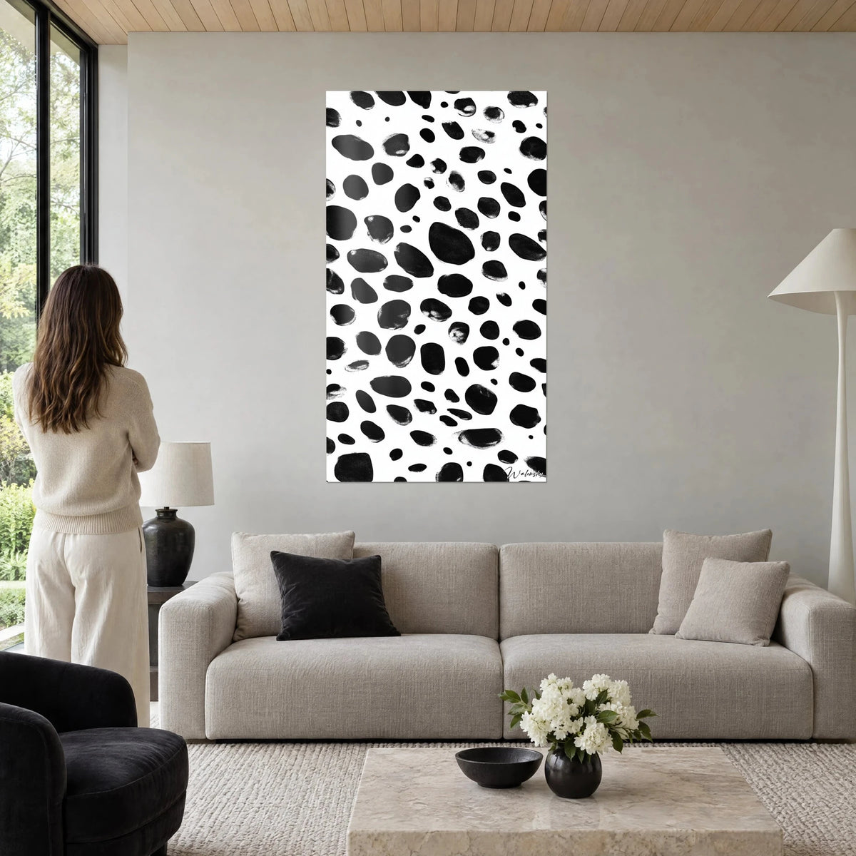 Tableau motif tacheté noir et blanc, taches d'encre ovales sur fond blanc, femme de dos, au-dessus d'un canapé dans un salon lumineux