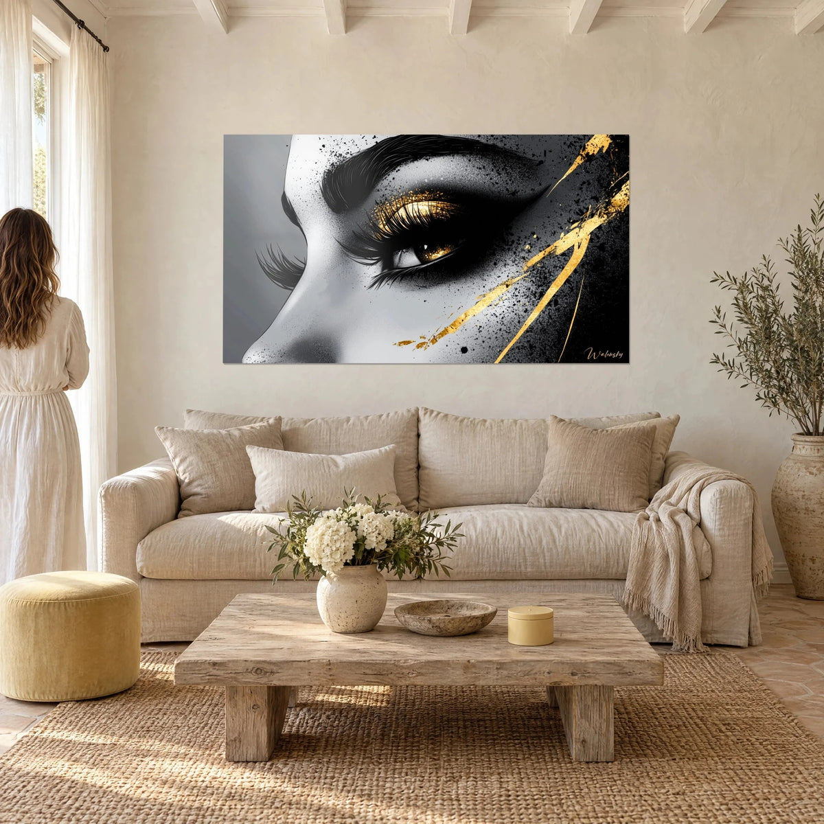 Schilderij met goudkleurig opgemaakt oog, zwarte wimpers en inktspatten, silhouet van achteren, boven een bank in een lichte woonkamer