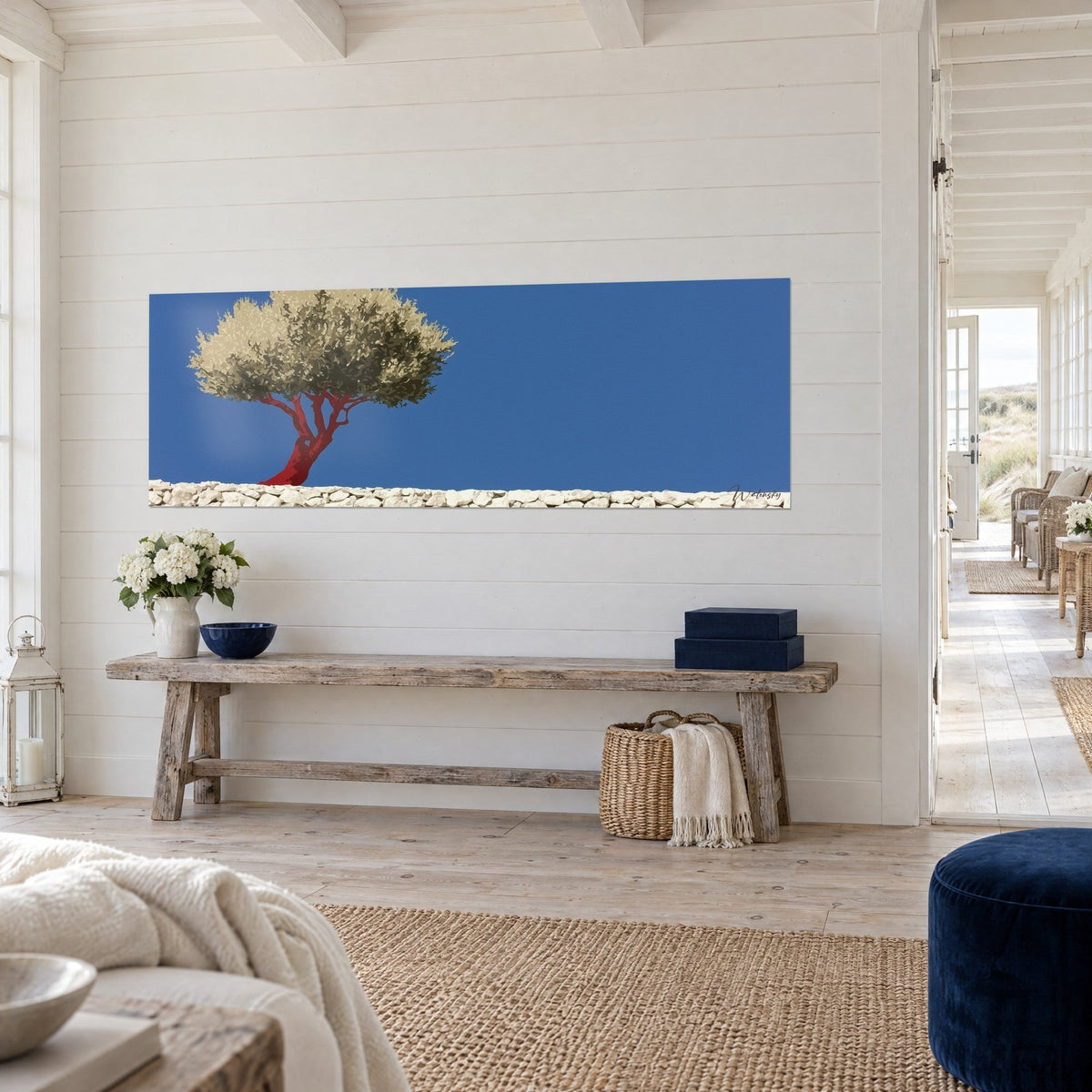 Cuadro de árbol mediterráneo con tronco carmín junto a un muro de piedras blancas y cielo azul, vista de tres cuartos, consola de madera