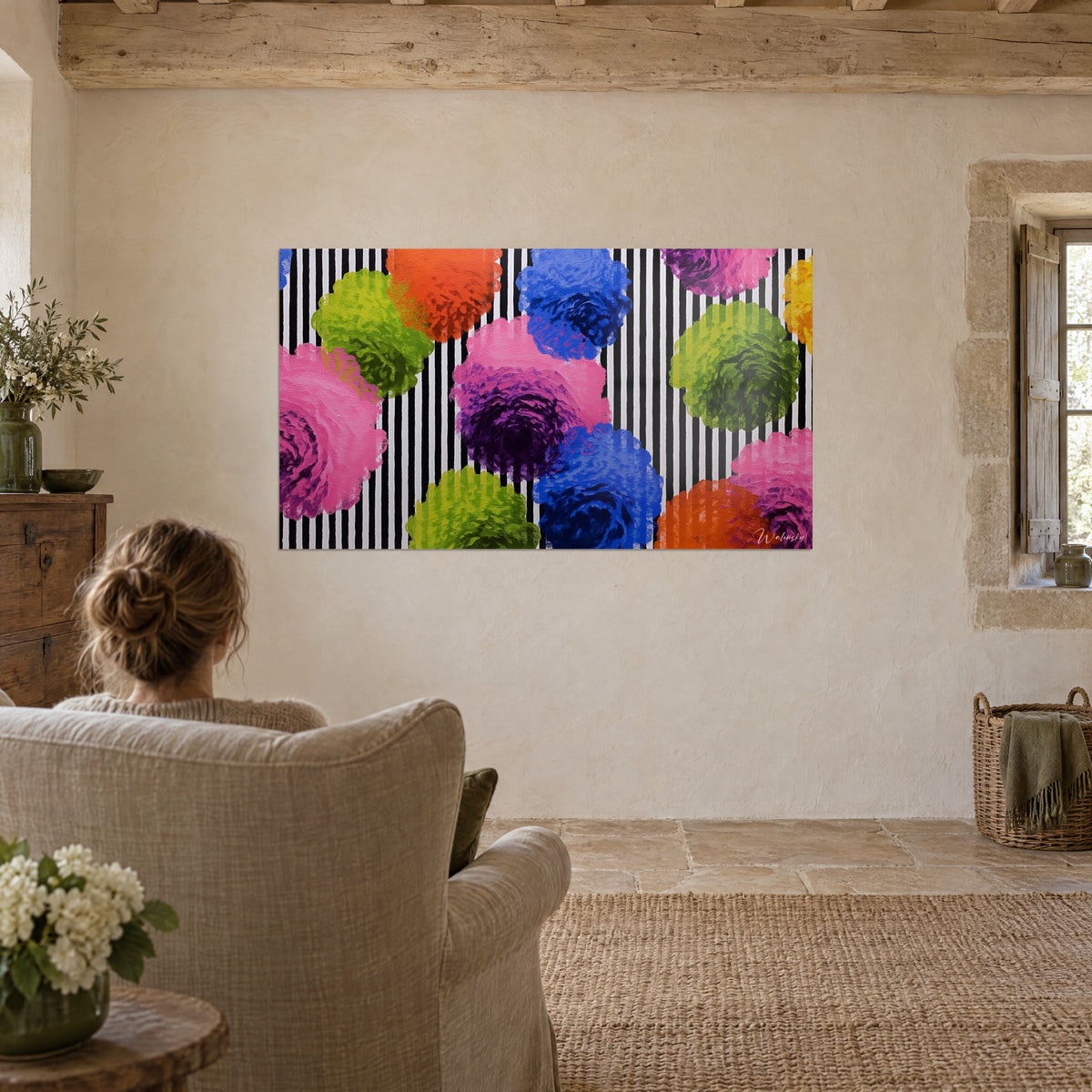 Wall art multicoloured round trompe-l'œil flowers on black and white stripes, woman seen from behind seated in a linen armchair, beige wall