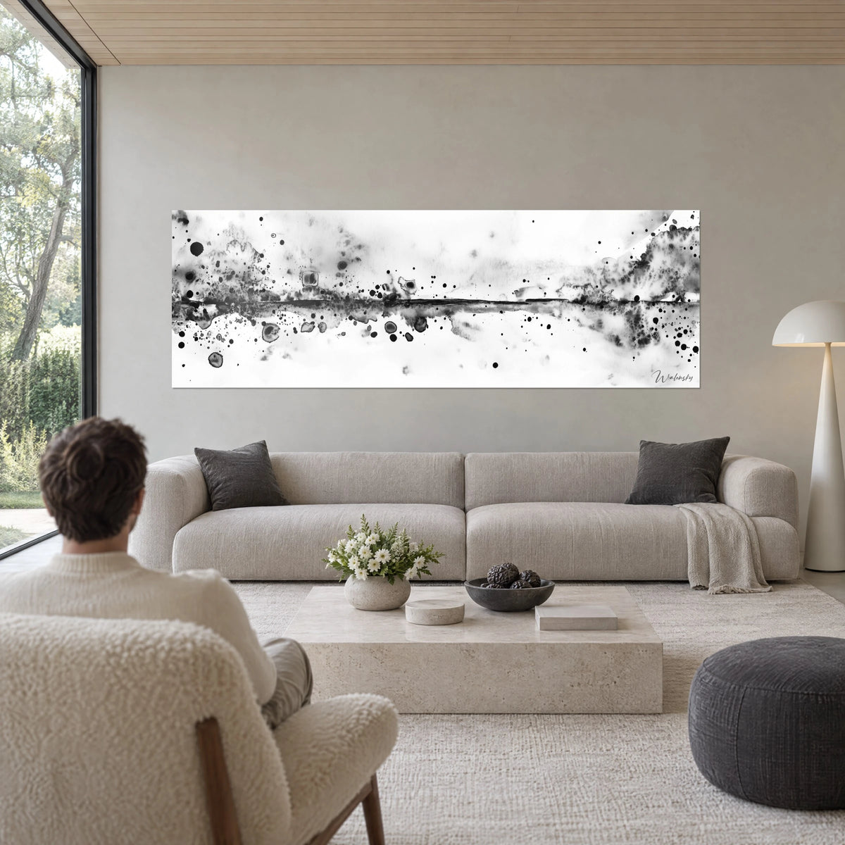 Schilderij met zwarte inktwas gespetterd op witte achtergrond, donkergrijze horizon en zwarte druppels, boven een bank in een lichte woonkamer