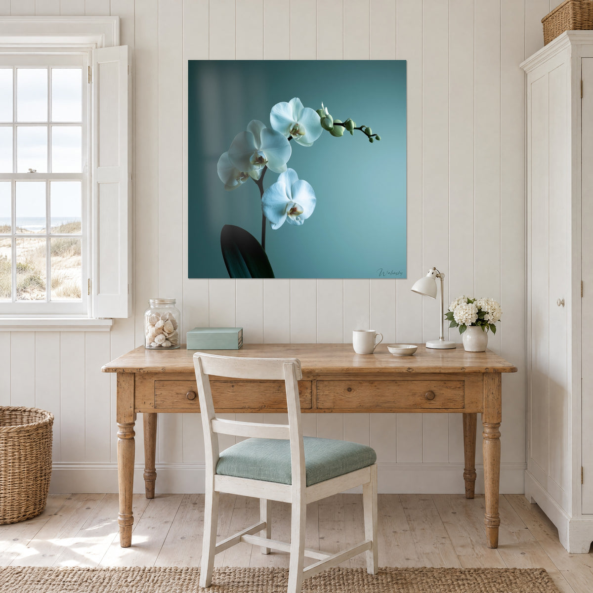 Cuadro orquídea mariposa blanca, corazón rosado y fondo azul glaciar, colgado encima de un escritorio de madera clara y una silla