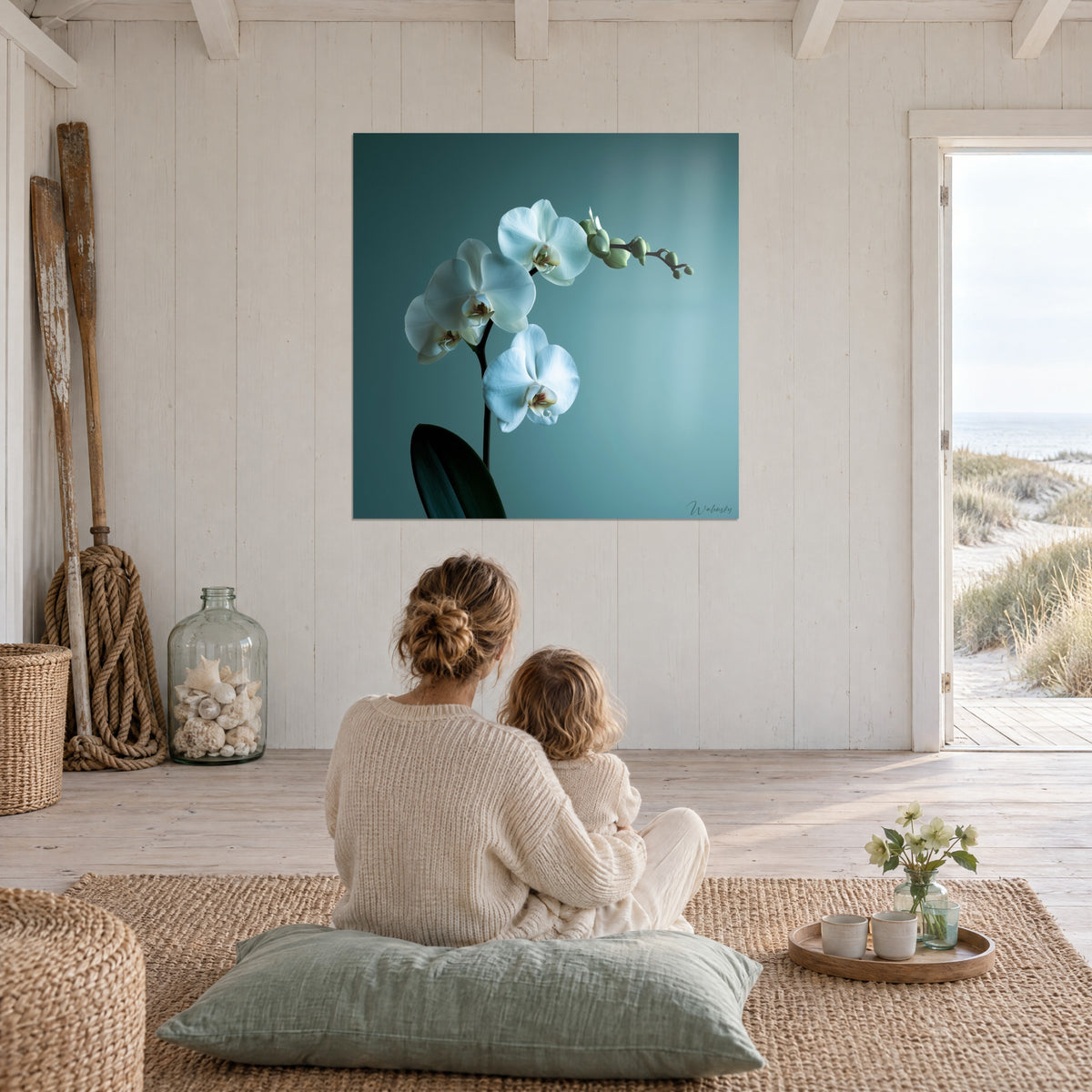 Cuadro rama de orquídea blanca, fondo azul verdoso suave, madre e hijo de espaldas sobre una alfombra de yute, encima de una estancia abierta a la playa