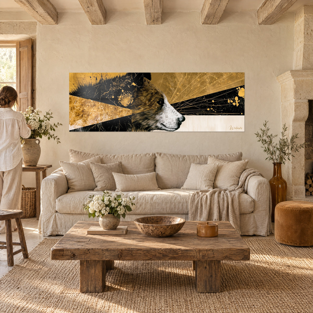 Tableau ours brun de profil, museau blanc, fond noir et or éclaboussé, personne de dos, au-dessus d'un canapé dans un salon lumineux
