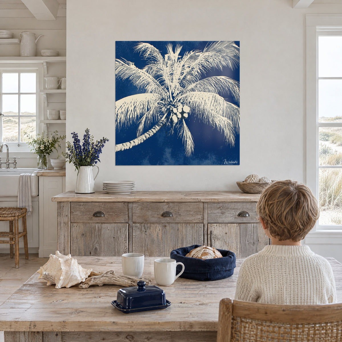 Wall art wreath of white palm fronds on royal blue background, clustered coconuts, in front of a child seated at a light wood table