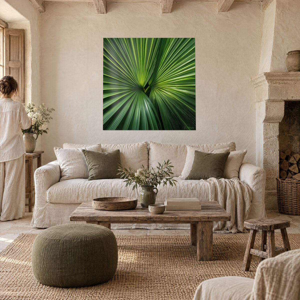 Schilderij waaiervormig palmblad met levendig groene en gele nerven, een vrouw van achteren, boven een bank in een lichte woonkamer