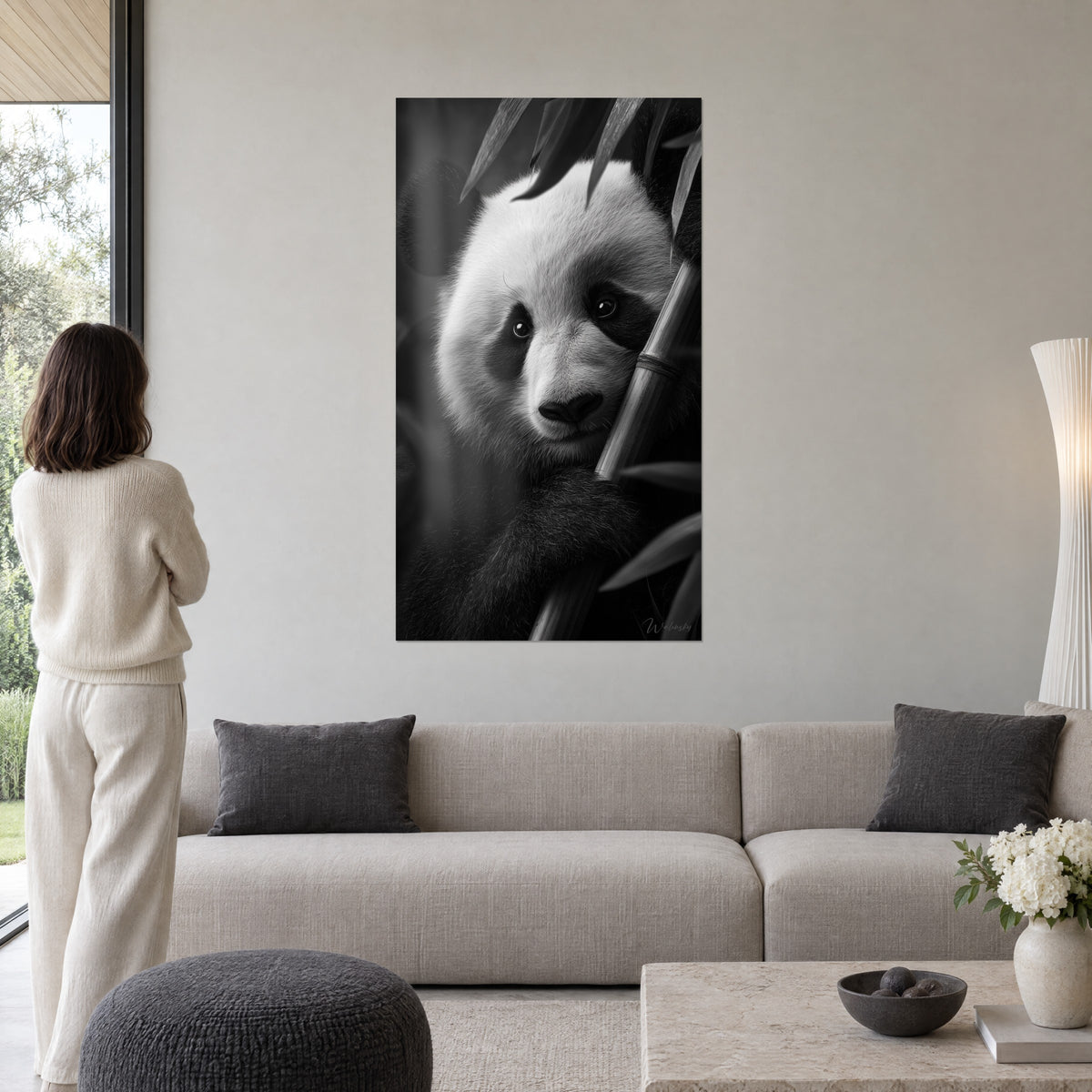 Cuadro de un panda gigante en blanco y negro, mirada apoyada contra un tallo de bambú, pelaje marfil y carbón, sobre un sofá en un salón luminoso