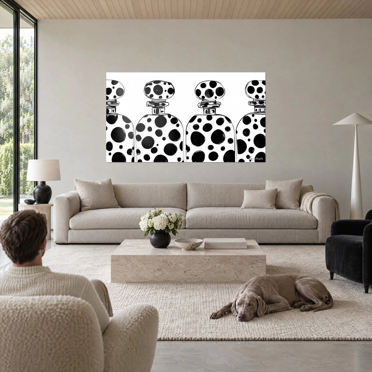 Wall art perfume bottles with black dots on white background, round stoppers, man seen from behind and Weimaraner above a sofa in a bright living room