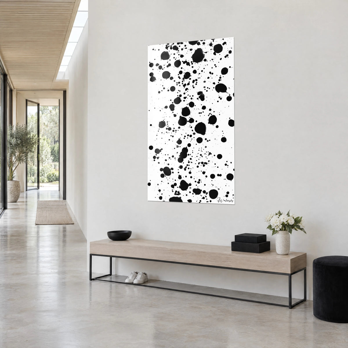 Gemälde mit schwarzen Tintentropfen auf reinem Weiß, Dreiviertelansicht an einer hellgrauen Wand, beige Holzbank und weiße Blumen