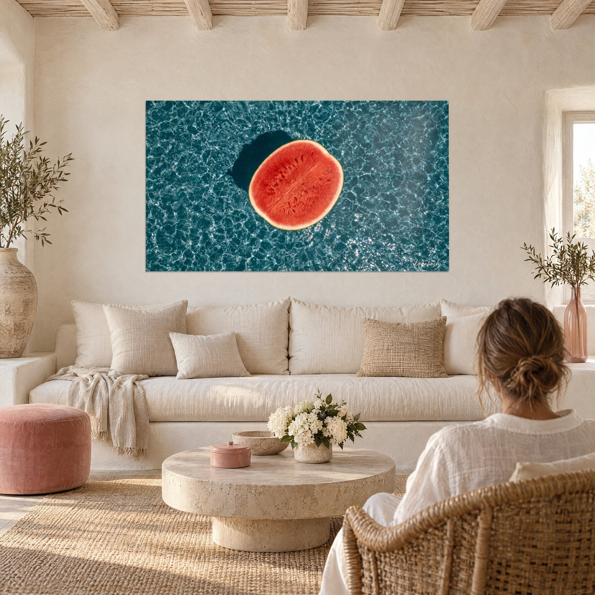 Wall art halved watermelon coral red floating on rippled petrol-blue water, dark shadow, above a sofa in a bright living room