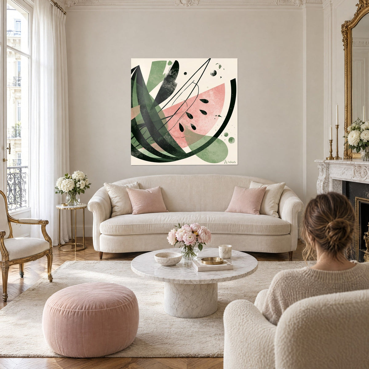 Gemälde abstrakte rosa Wassermelonenscheibe, schwarze Kerne und salbeigrüne Blätter, zwei Personen von hinten, über einem Sofa in einem hellen Wohnzimmer aufgehängt