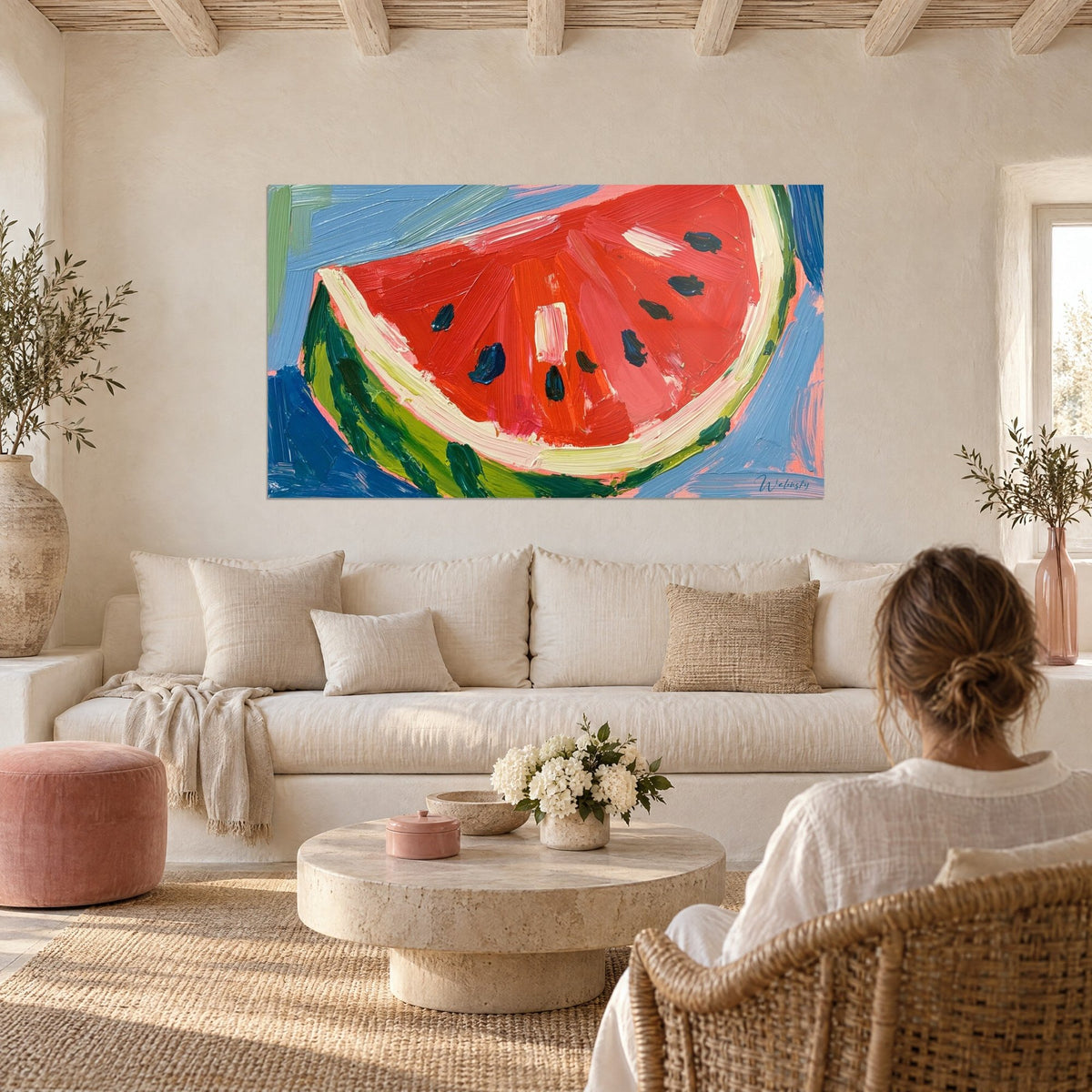 Wall art of a bright red and sky blue watermelon slice, navy seeds cut with a knife, above a sofa in a sunlit living room