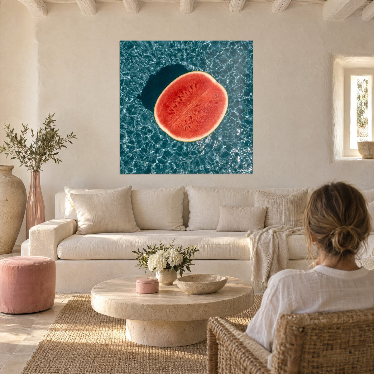 Wall art of a halved red watermelon floating on turquoise water, silver reflections, hung above a sofa in a bright living room