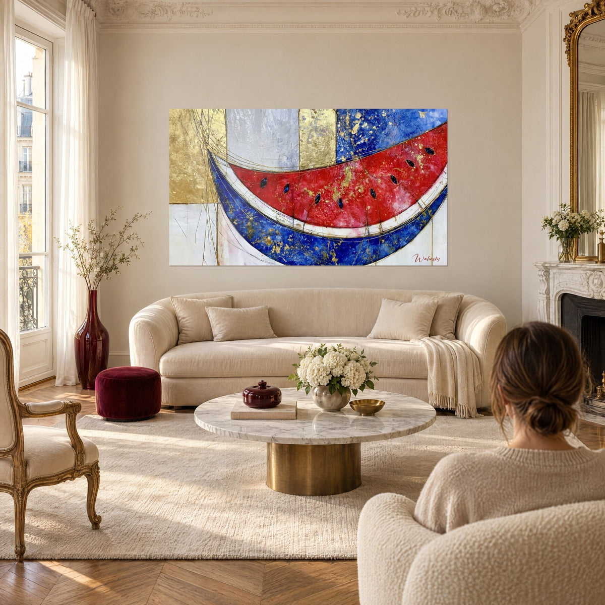 Tableau tranche de pastèque rouge vif et bleu marine, feuilles d'or éclatées, deux femmes de dos, au-dessus d'un canapé dans un salon lumineux