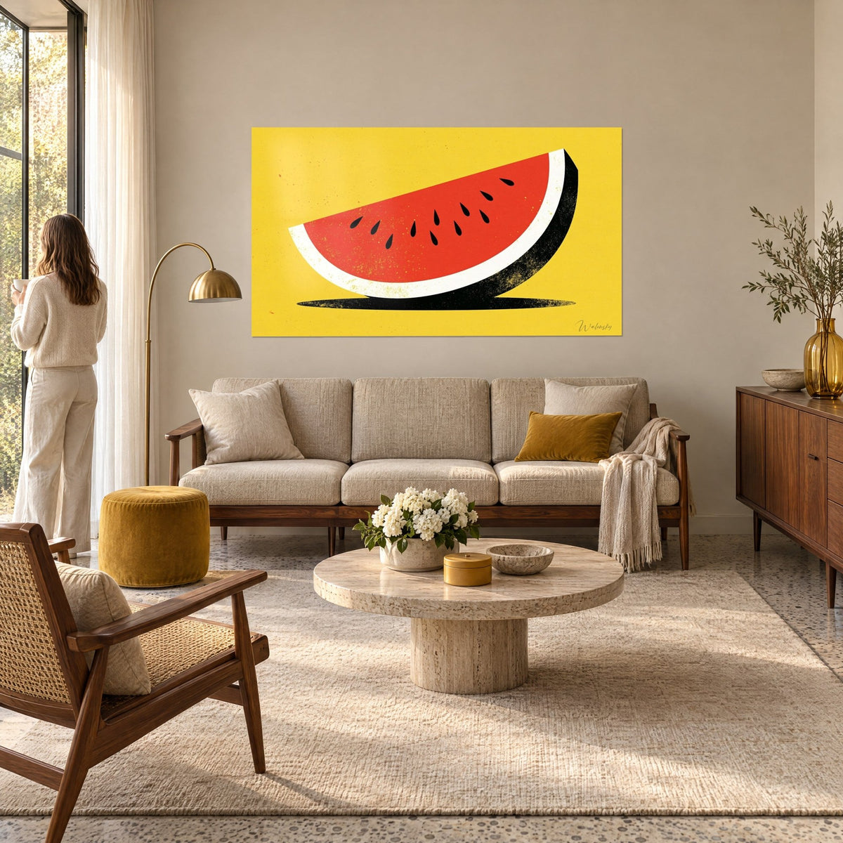 Wall art watermelon wedge in vermilion red on mustard yellow background, black seeds in droplet shapes, above a sofa in a bright living room