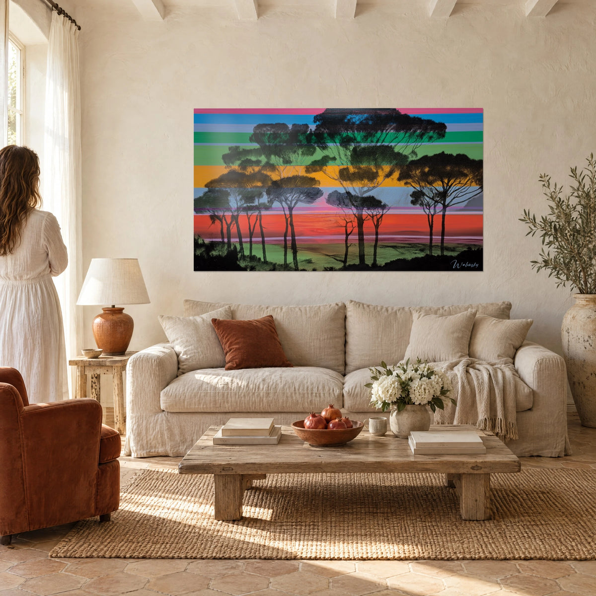 Wall art pine parasol trees as black shadows on pink, blue and green stripes, woman seen from behind above a sofa in a bright living room
