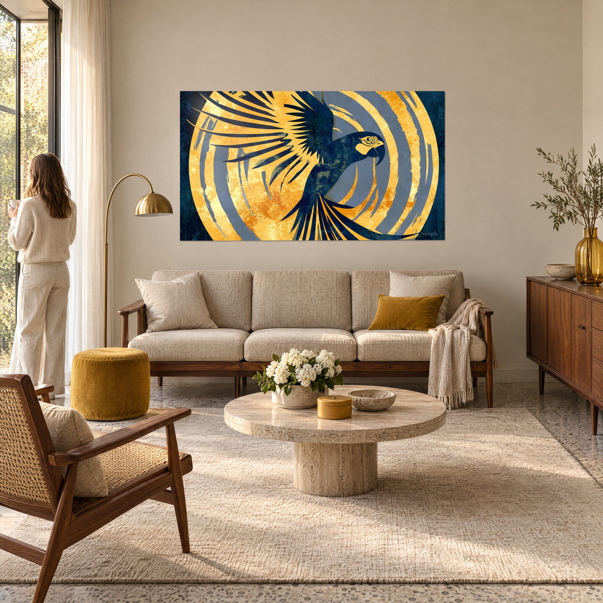 Wall art navy blue macaw with wings spread over a golden disc, grey-blue circles; woman from behind, above a sofa in a bright living room