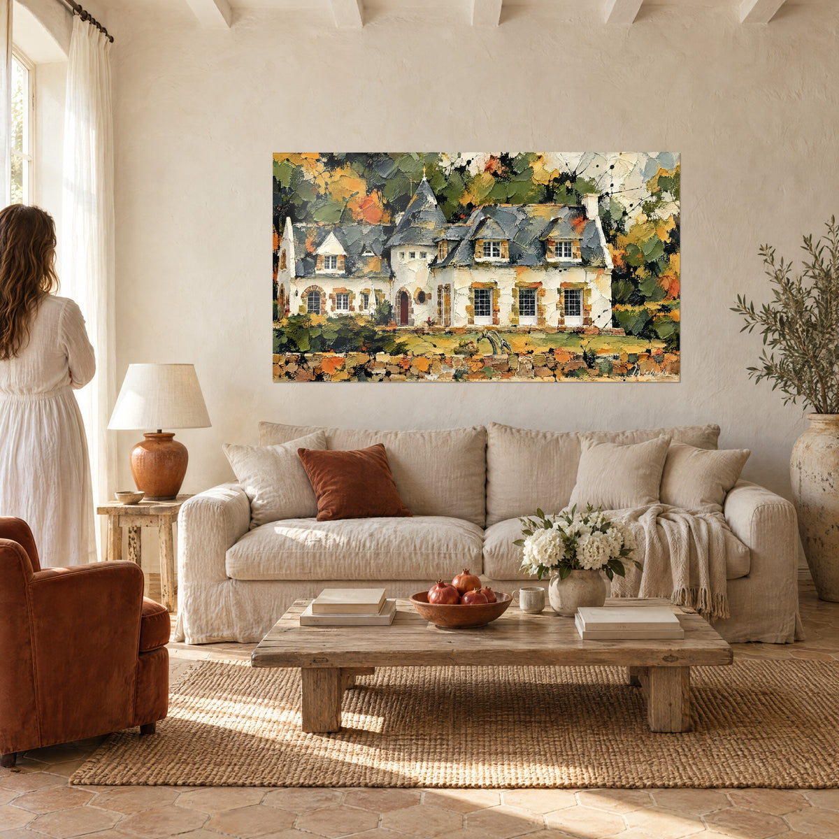 Tableau manoir blanc à tourelle d'ardoise grise, murs crépis crème et feuillages orange, au-dessus d'un canapé dans un salon lumineux