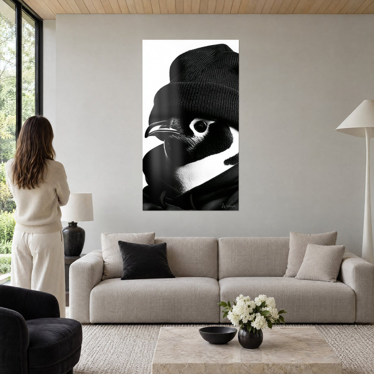 Gemälde Pinguin in Schwarzweiß mit gestricktem schwarzem Beanie, glänzender Schnabel, runder Auge, Frau von hinten, über einem Sofa in einem hellen Wohnzimmer