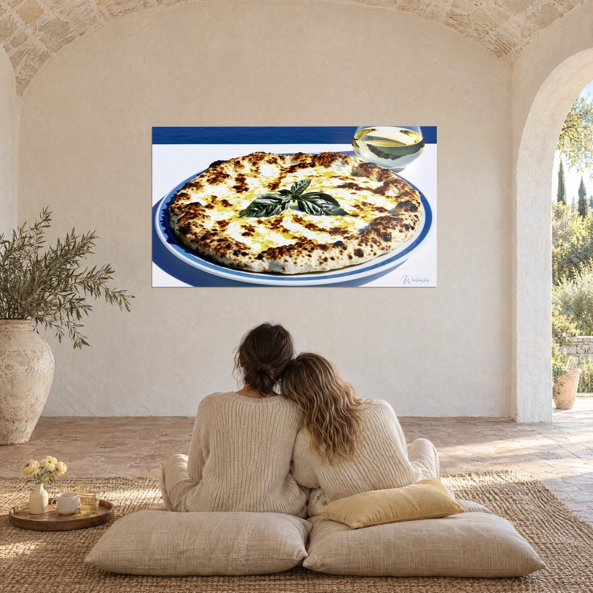 Obraz złota pizza z bazylią, lazurowy talerz na białym obrusie, dwie osoby tyłem siedzące na poduszkach, prowansalski salon