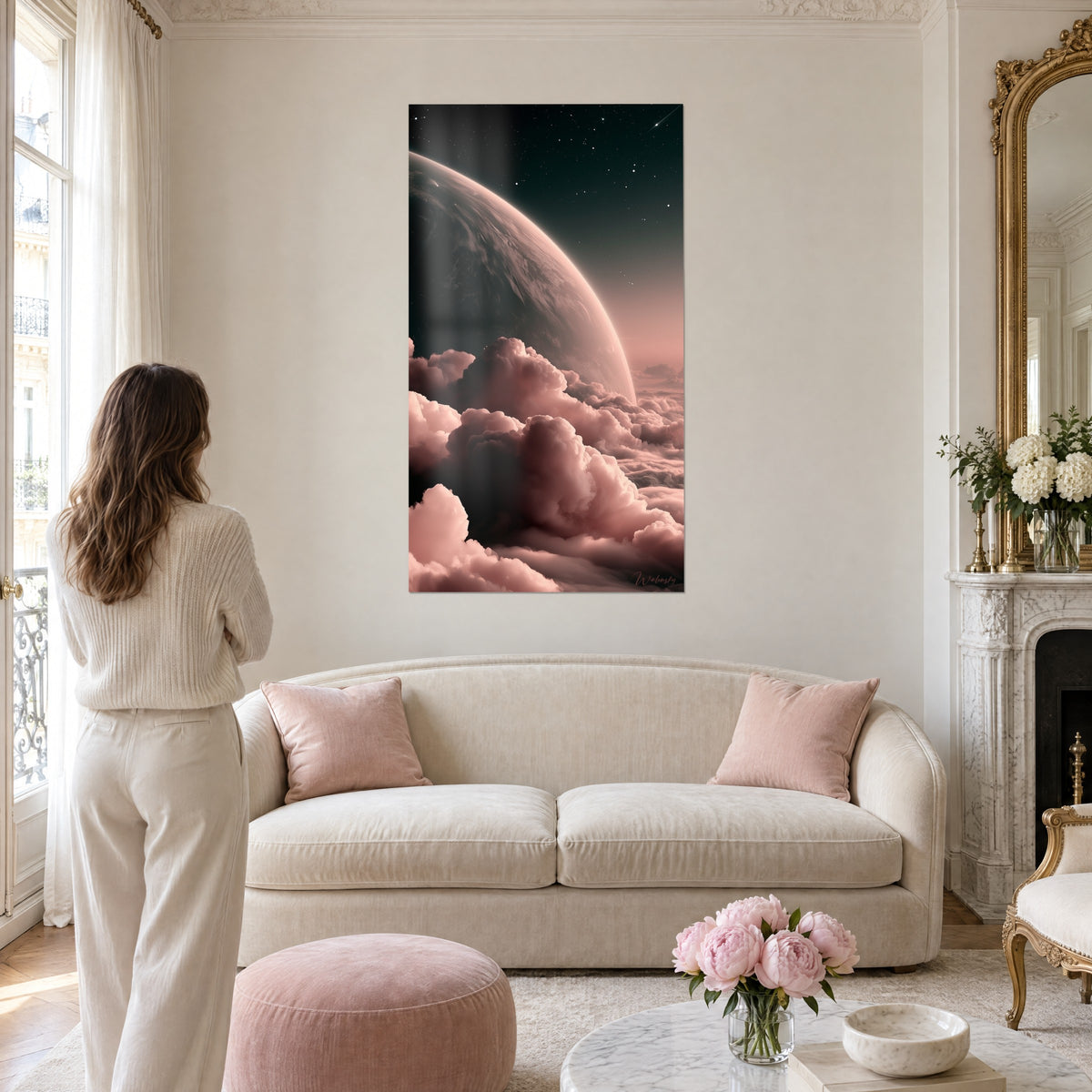 Schilderij donkere planeet die oprijst uit een zee van poederroze wolken, witte sterren, vrouw van achteren boven een bank in een lichte woonkamer