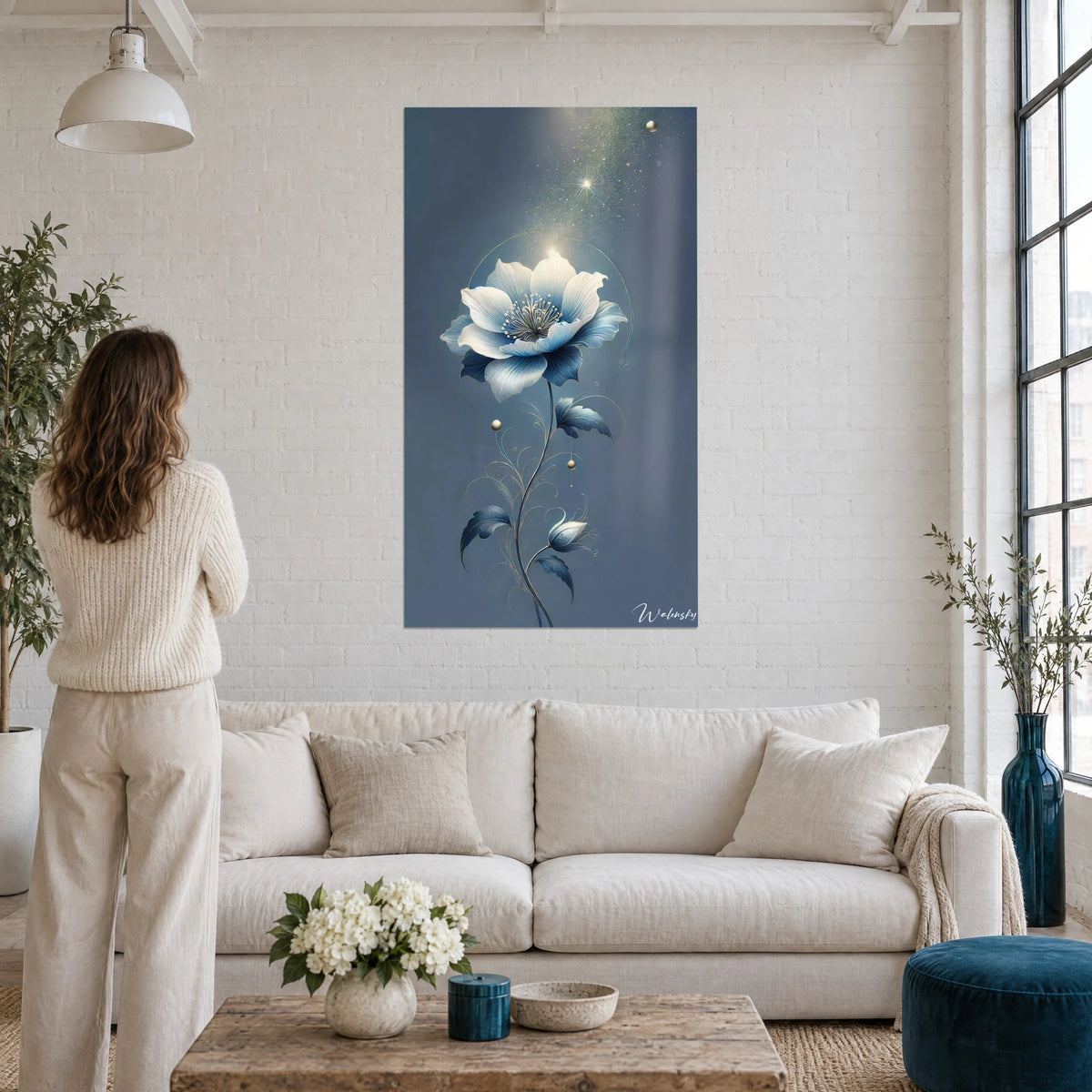 Tableau fleur nacrée aux pétales bleu acier sur fond ardoise, femme de dos, au-dessus d'un canapé dans un salon lumineux