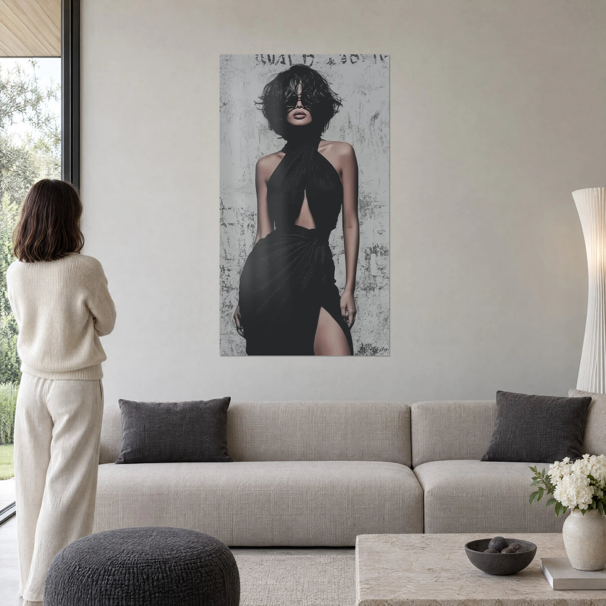Quadro donna bruna con occhiali da sole neri, abito nero incrociato con schiena nuda, parete grigia patinata, sopra un divano in un soggiorno luminoso