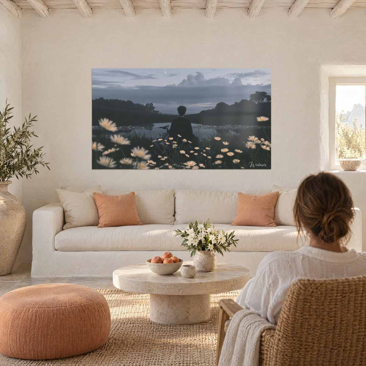 Wall art back-view silhouette on a quad bike, cream daisies and grey water at dusk, hung above a sofa in a bright living room