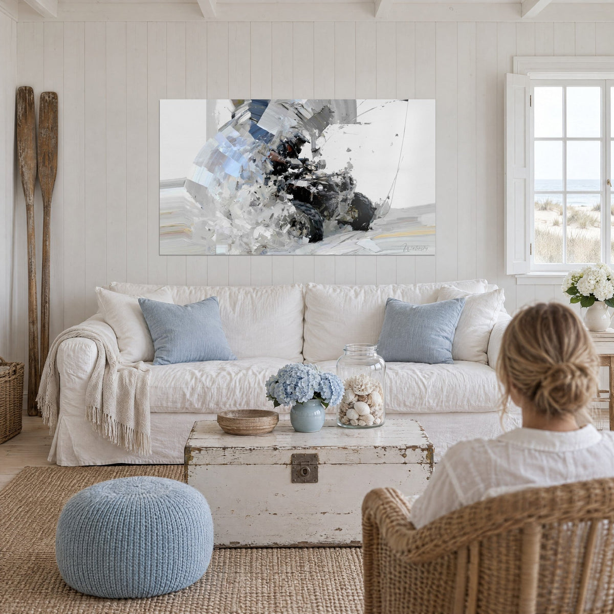 Wall art of a black quad rider plunging through a burst of white and glacier-blue snow, above a sofa in a bright living room