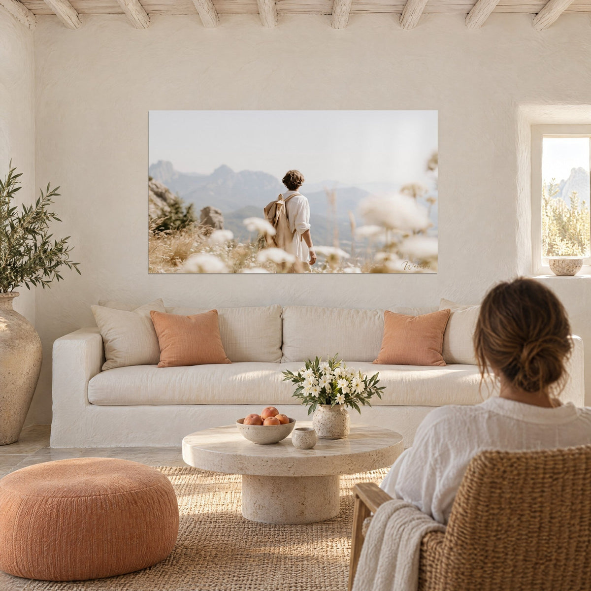 Tableau randonneur de dos au sac beige dans les fleurs blanches, montagnes bleutées, au-dessus d'un canapé dans un salon lumineux