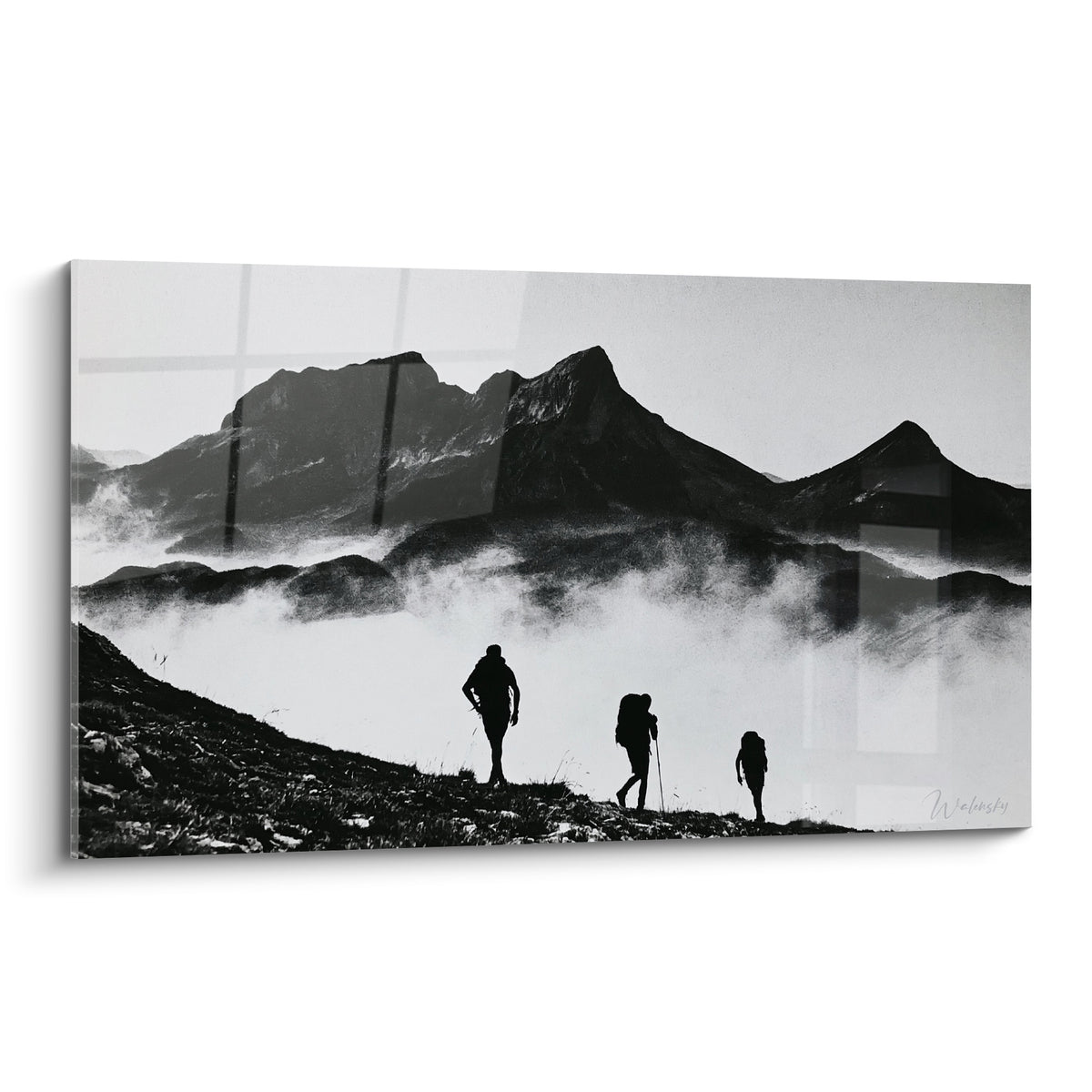 Trois randonneurs en silhouette noire gravissent une crête grise dans la brume, sommets sombres à l'arrière-plan