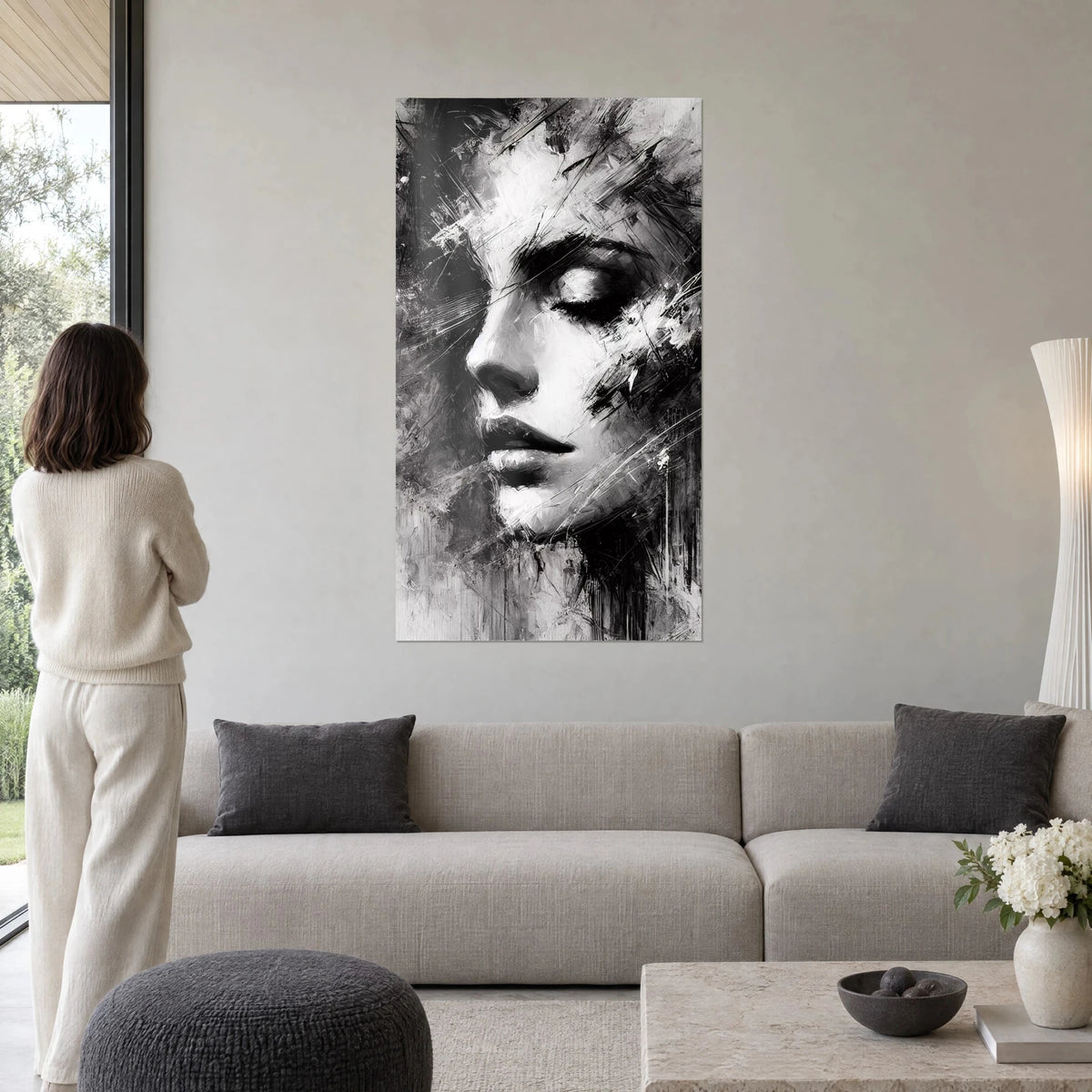 Tableau visage de femme aux yeux clos en noir et blanc, coups de brosse gris perle, femme de dos au-dessus d'un canapé dans un salon lumineux