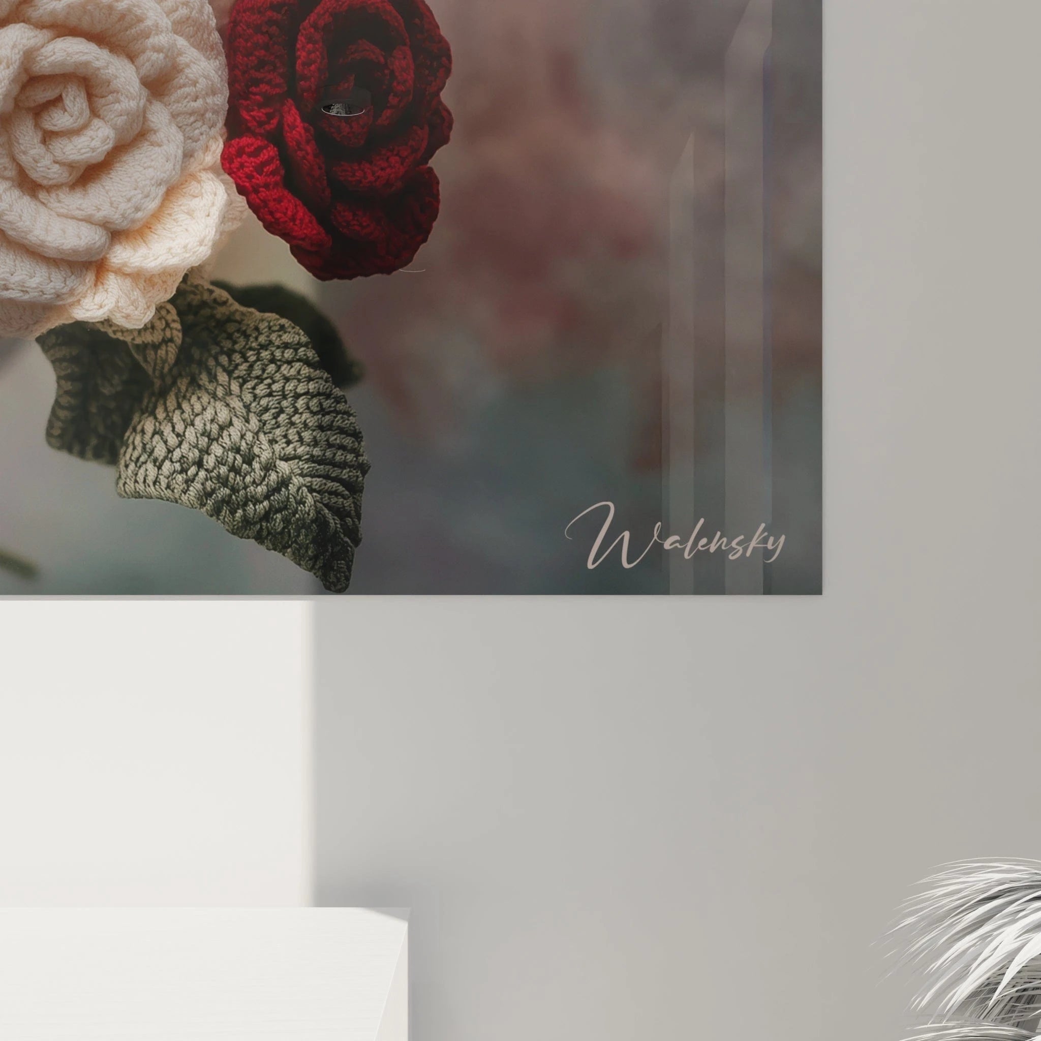 Un tableau crochet floral exhibant un assemblage serré de roses tricotées en fil rouge, blanc et rose pâle, chaque fleur présentant des détails minutieux de pétales superposés et des feuilles vertes texturées, formant une composition équilibrée et raffinée.