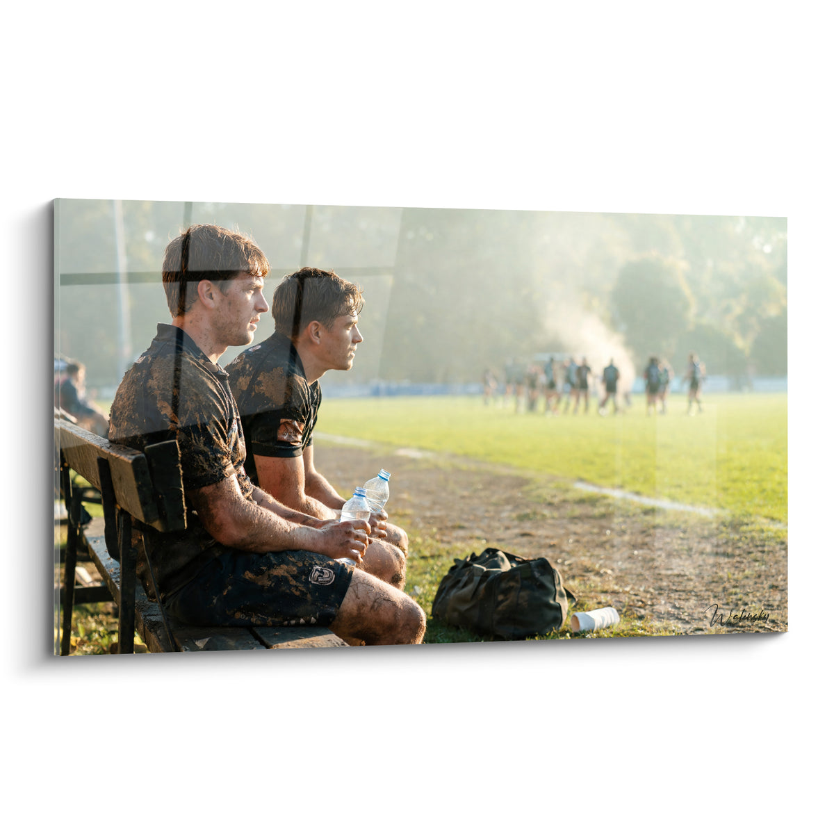 Joueurs de rugby aux maillots noirs et ocre, assis sur un banc face au terrain brumeux